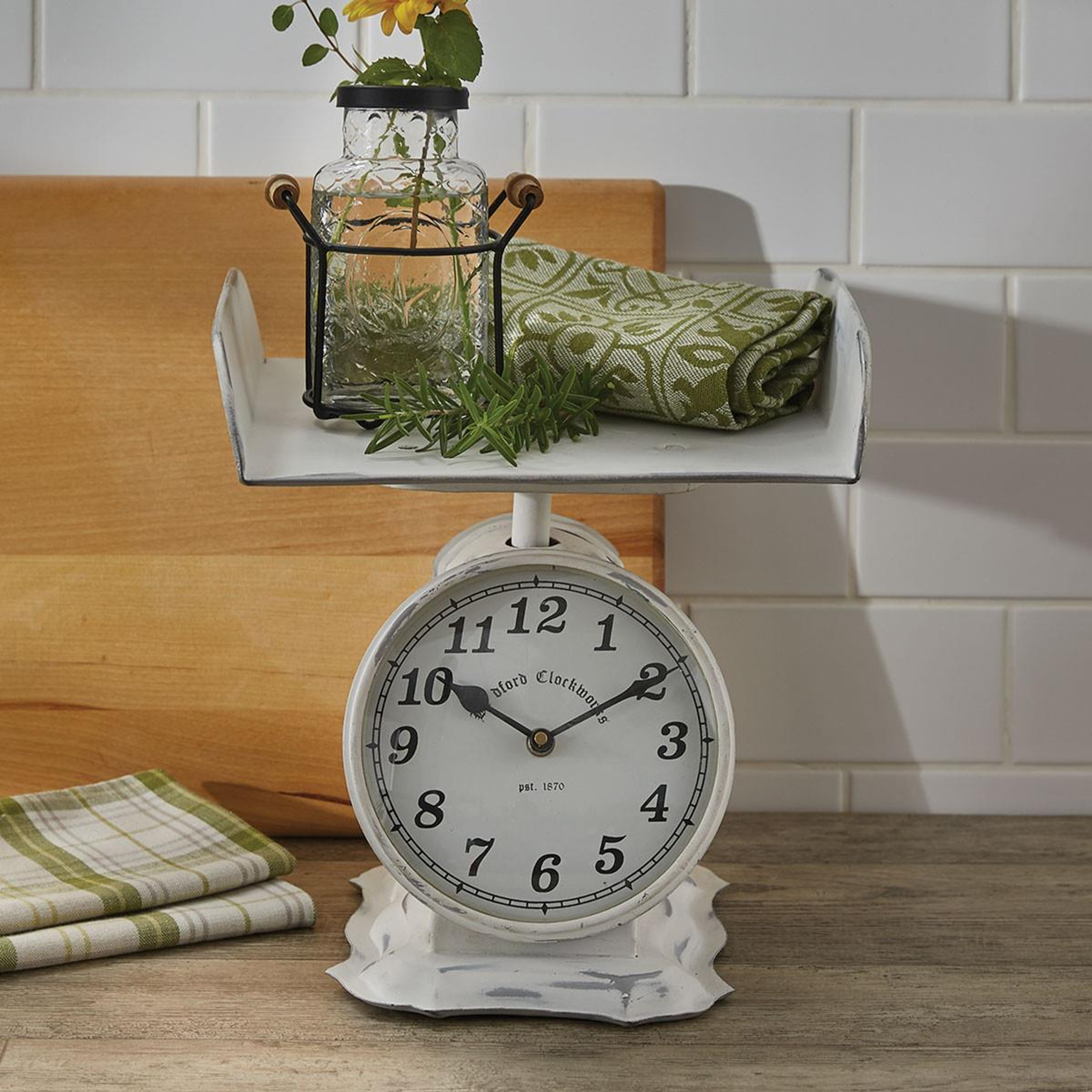 Baby scale clock holding a vase of flowers and a washcloth